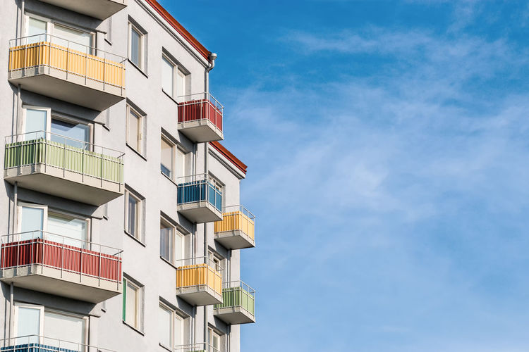 A light gray clean and tidy house building with colored balconies against a colorful blue sky. 
