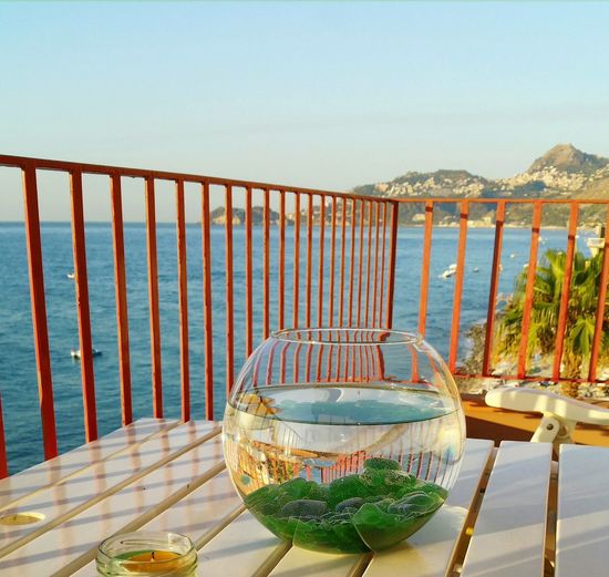 Fish bowl on table by sea against clear sky