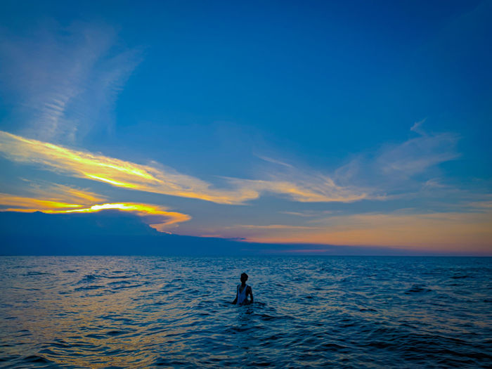 Man swimming in sea against sky during sunset