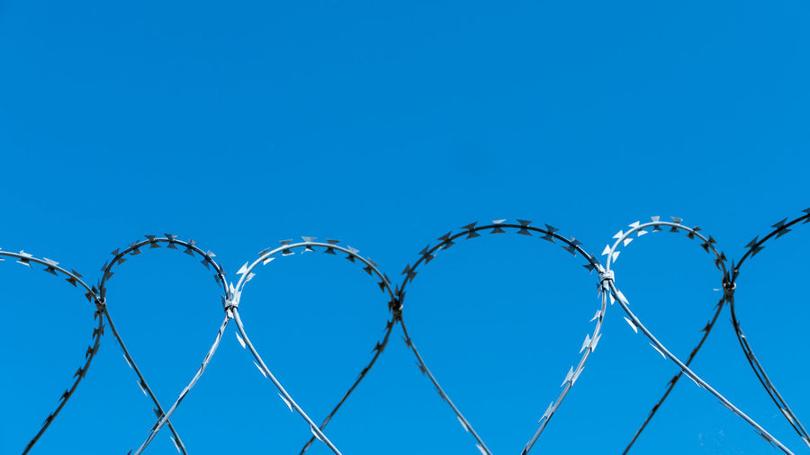 Low angle view of razor wire fence against clear blue sky