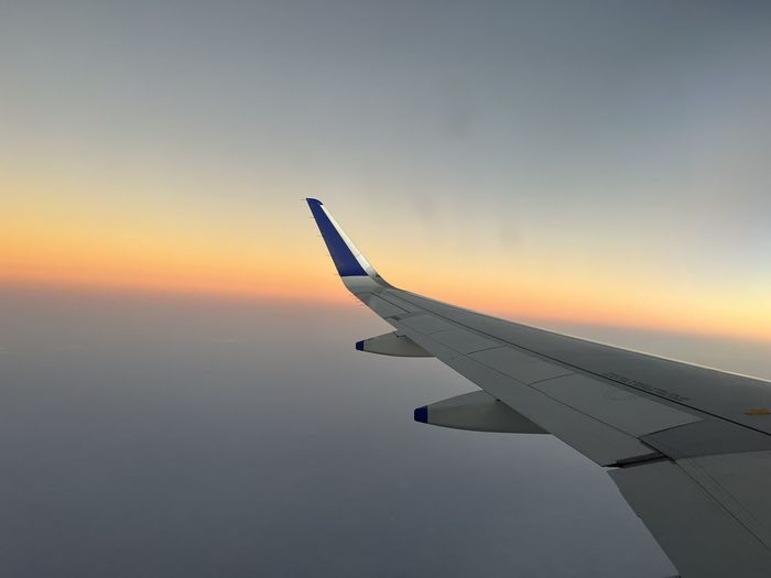 Cropped image of airplane wing against sky during sunset