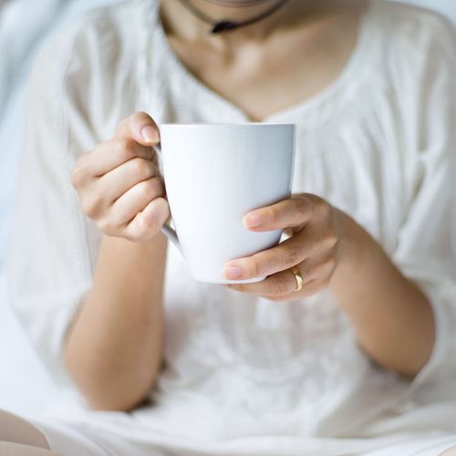 Woman holding coffee cup on bed