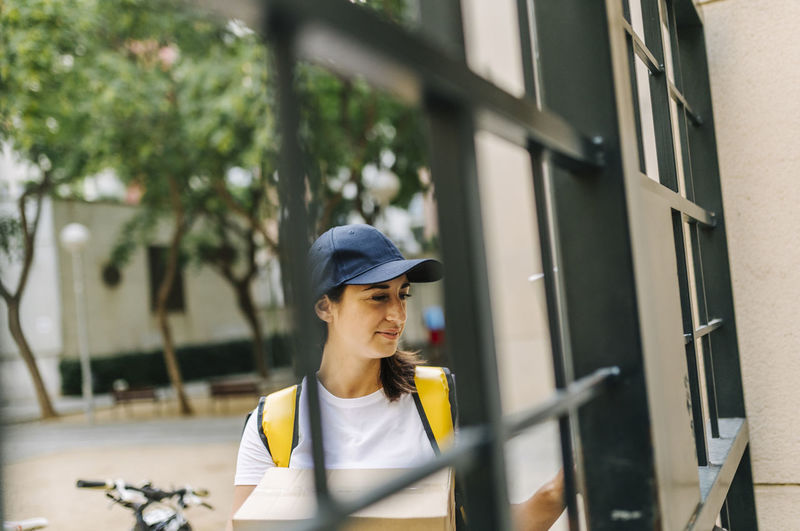 Female delivery person holding package while standing at gate