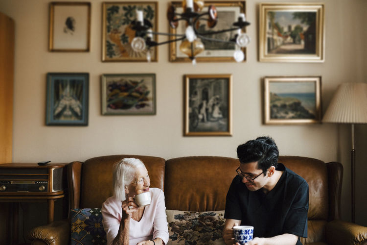 Male caregiver having coffee with elderly woman in living room