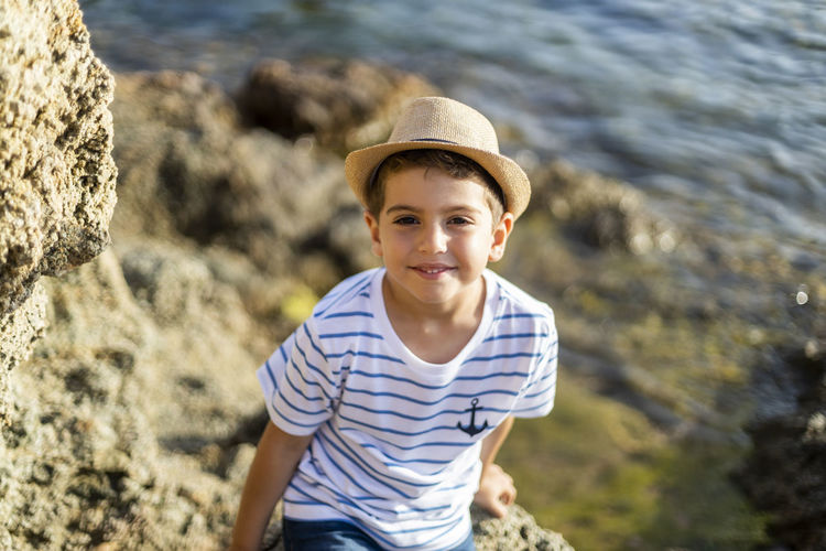 Portrait of smiling boy sitting on rock against sea