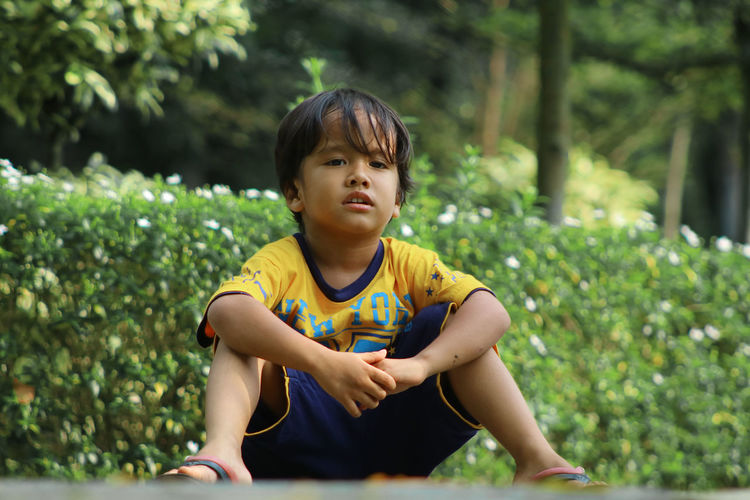 Portrait of boy sitting against plants