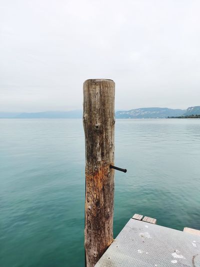 Wooden post on pier by sea lake against sky