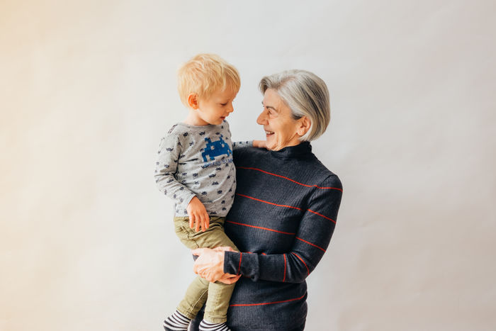 Smiling grandmother carrying grandson while standing against wall