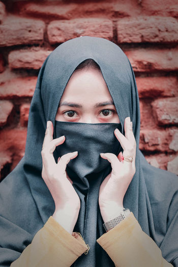 Close-up portrait of young woman covering face against wall