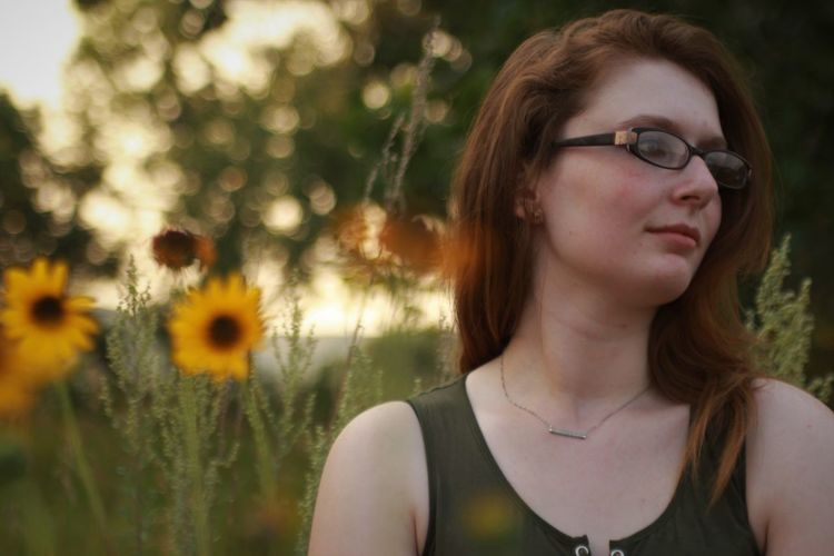 Thoughtful young woman wearing eyeglasses while looking away on land during sunset