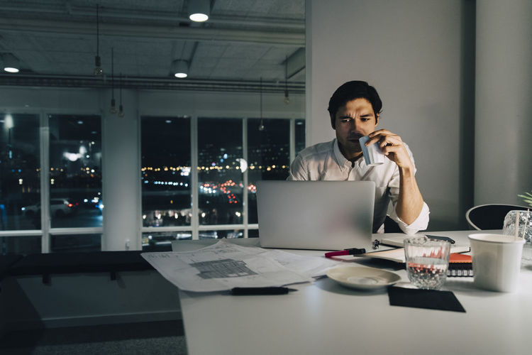 Dedicated businessman holding coffee cup while working late at office