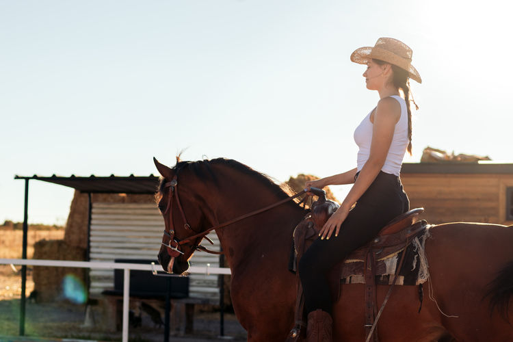 Side view of young woman riding horse against sky