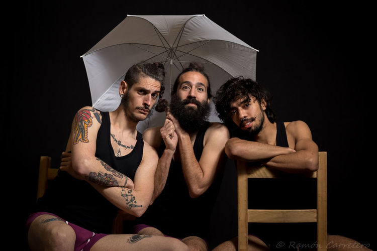 Portrait of friends sitting with umbrella against black background