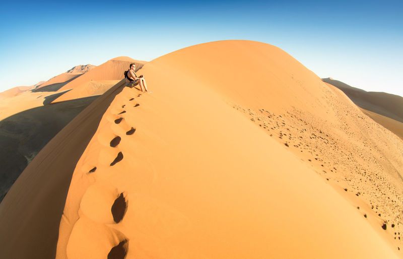 Man sitting on sand dune at desert