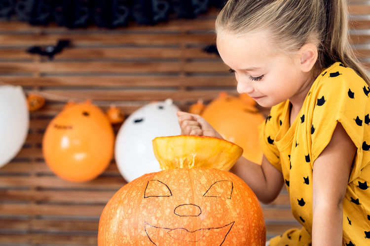 Close-up of cute girl sitting by pumpkin at home