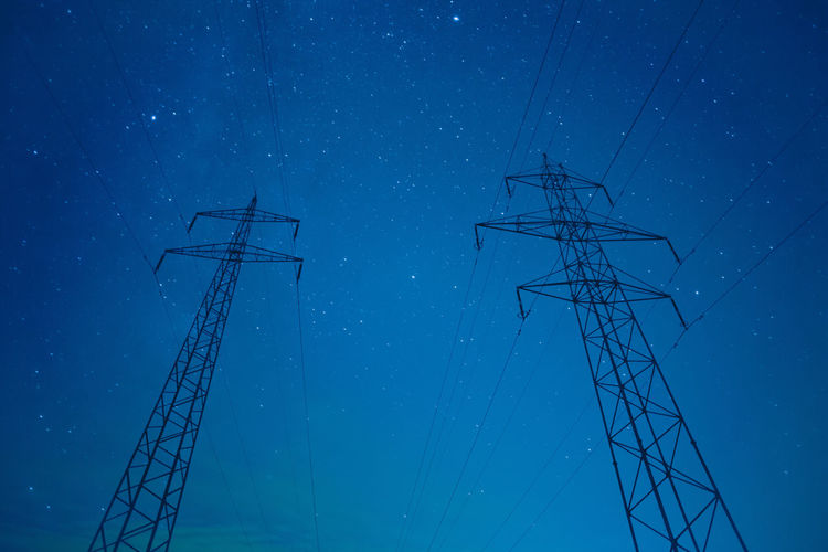 Low angle view of silhouette electricity pylons against star field at night