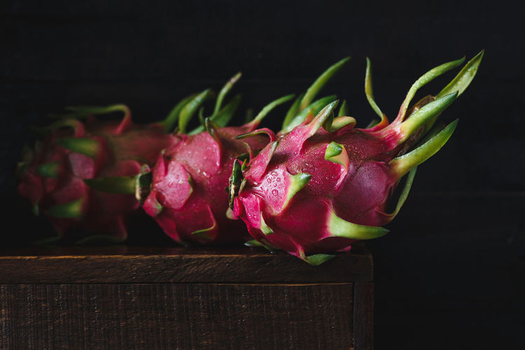 Close-up of wet dragon fruits on wood against black background
