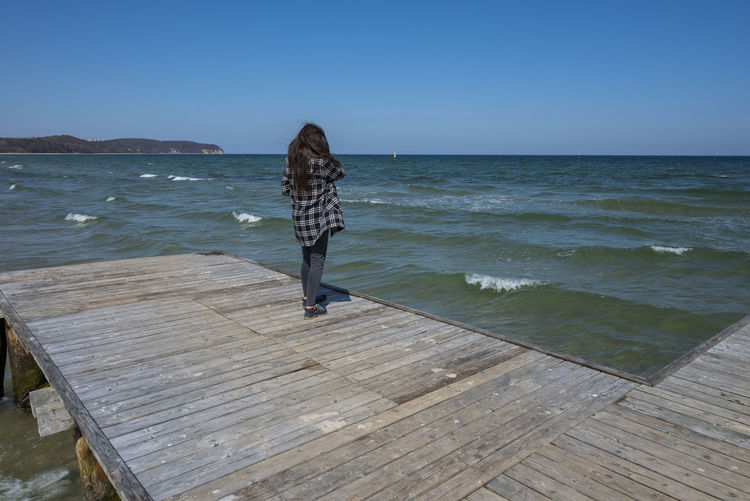 Rear view of woman walking on pier over sea against clear sky