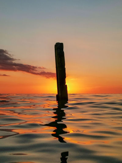 Wooden post in sea against sky during sunset