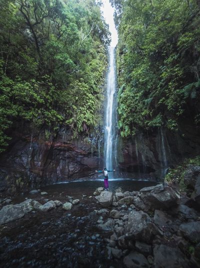 Scenic view of waterfall in forest with woman standing in front for scale