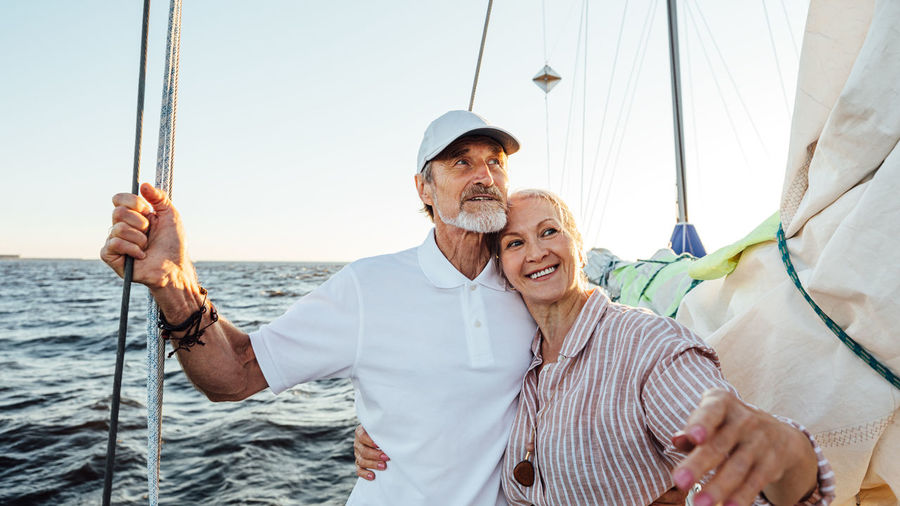 Smiling senior couple on sailboat in sea against sky