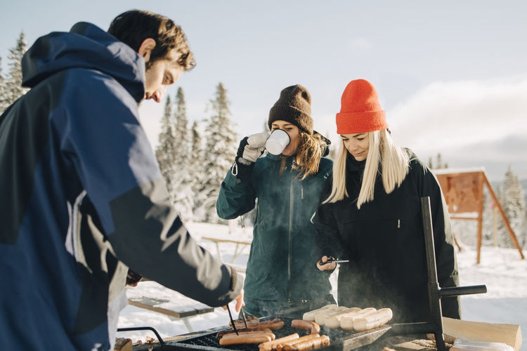 Man preparing sausages while female friends standing at ski resort