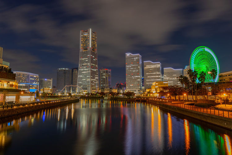 Illuminated modern buildings by river against sky at night in yokohama 
