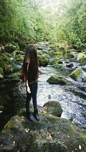 Young woman standing on rock by stream in forest