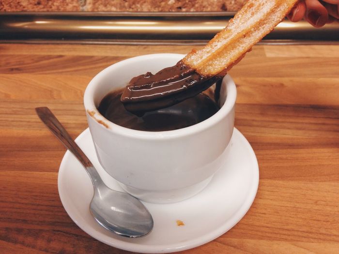 Cropped hand holding churro over hot chocolate