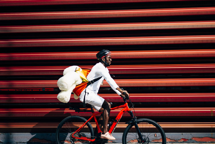 Bicycle courier delivering a teddy bear passing a red wall