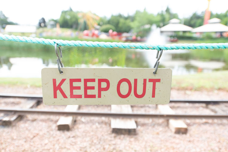 Close-up of keep out sign hanging on rope against railroad track