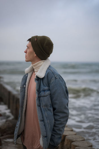Young man looking away while standing against sea