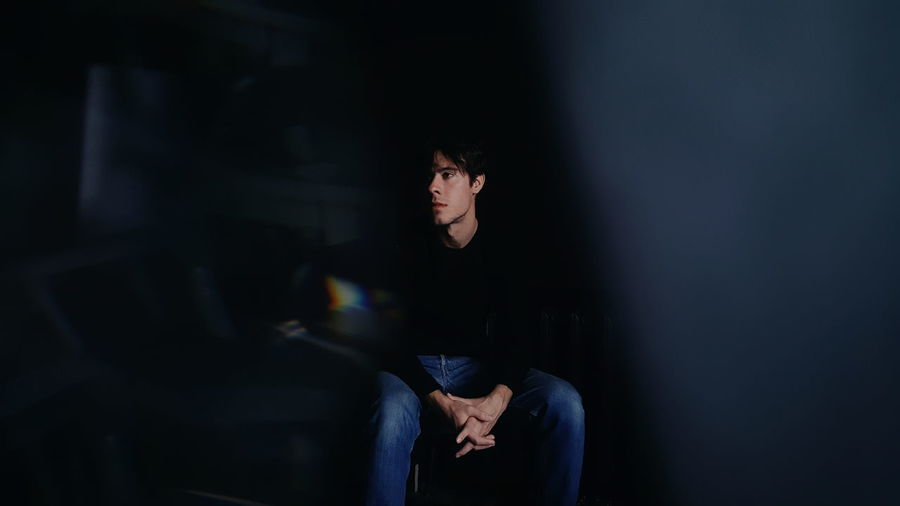 Thoughtful young man looking away while sitting on chair in darkroom