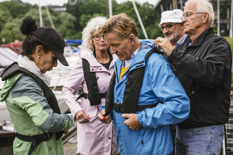 Senior man helping friend in wearing life jacket during boat master course