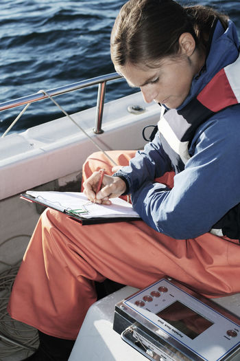 High angle view of woman examining while writing on clipboard in boat