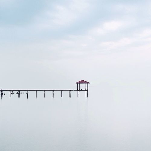 Gazebo on pier by calm lake against sky
