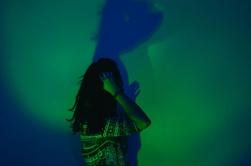 Woman standing against illuminated green wall with shadow