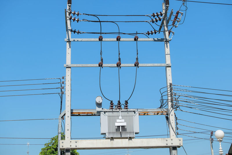 Low angle view of electricity transformer against clear blue sky