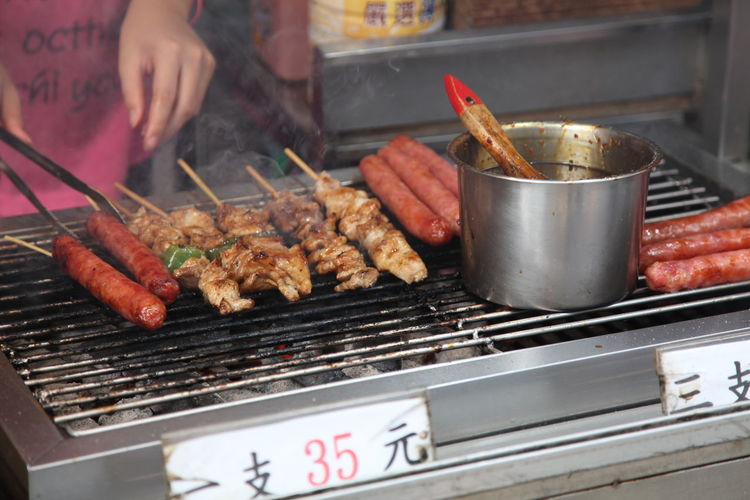 Midsection of person grilling sausages on barbecue grill at market stall