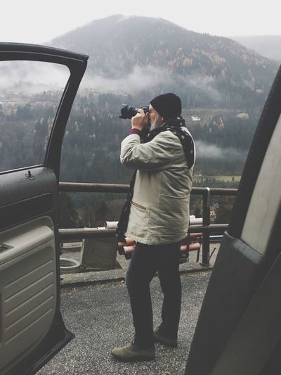 Full length of man photographing while standing by car against mountain