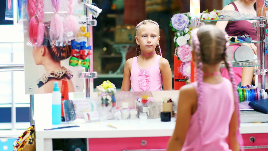 Beautiful blond girl, of seven years old, braided two pigtails, do a hairstyle with pink locks of