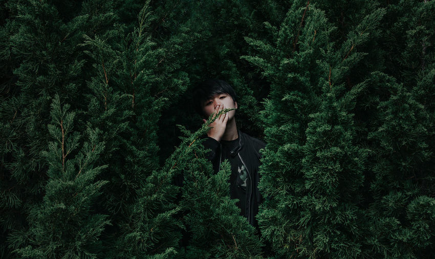 Portrait of man with hands covering mouth standing against trees