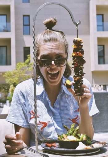 A woman with huge open mouth smile holding brazilian barbecue meat with her finger 