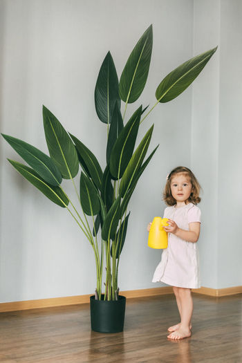 Little girl waters flowers at home, helps care for plants