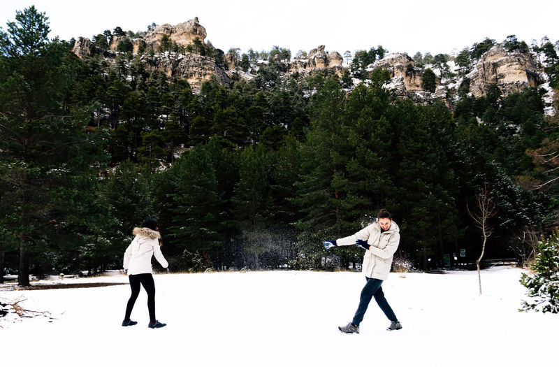 Two women throwing snowballs at each other in a natural snowy landscape.