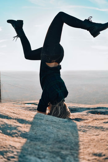 Full length of woman doing handstand on rock against sky