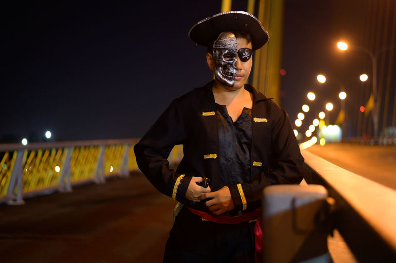 Portrait of young man wearing pirate costume standing on bridge at night