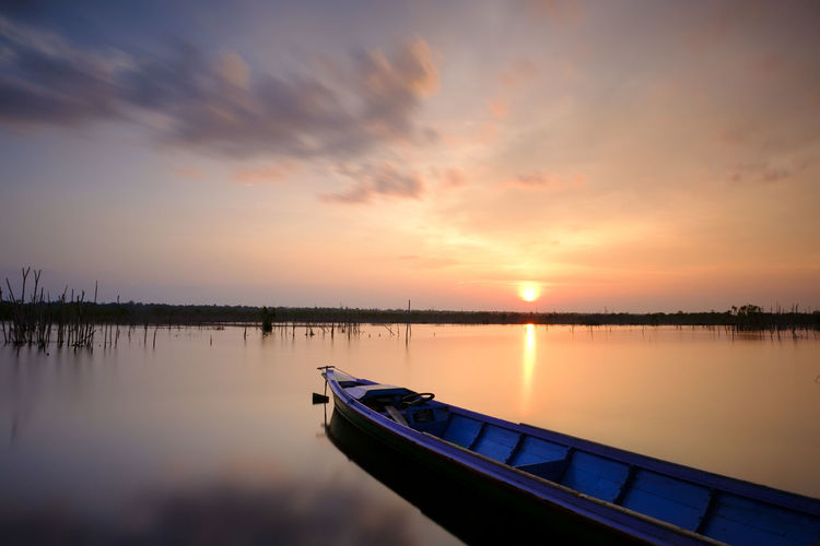 Boat moored in lake against sky during sunset