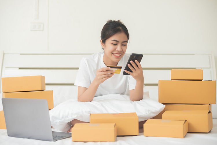 Young woman using phone while sitting in box