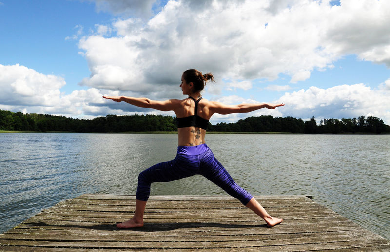 Rear view full length of young woman doing yoga on jetty by lake
